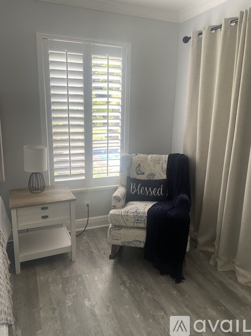 A chair with a blanket on it is in front of a window with blinds.