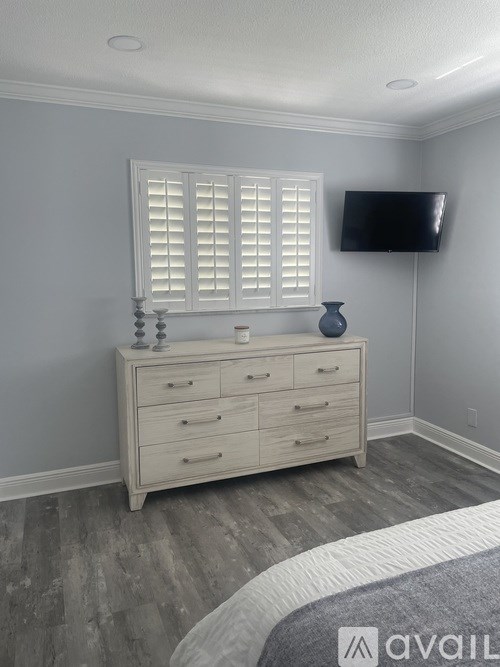 A bedroom with a white dresser and a window with white shutters.