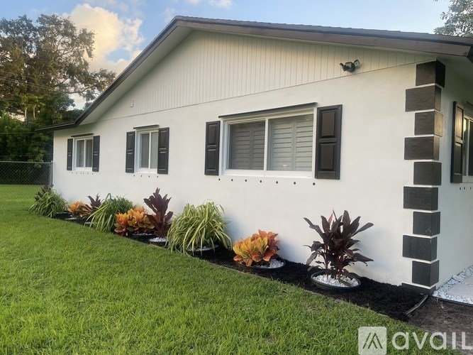 A white house with a striped pillar and a row of plants in front.