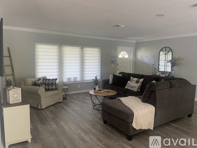 A living room with a couch, chair, ottoman, and a table with a vase of flowers on it.