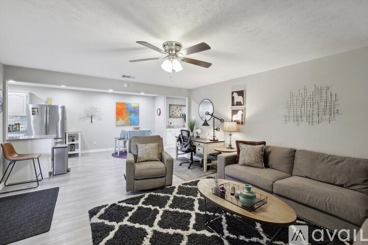 A living room with a grey couch, a black and white rug, and a ceiling fan.