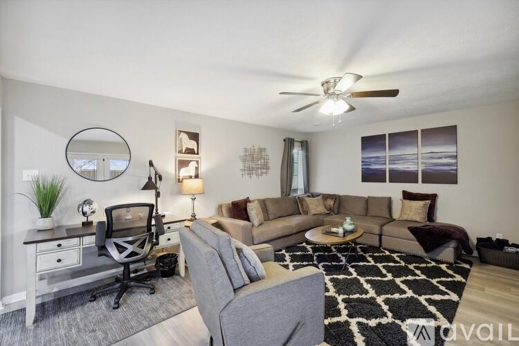 A living room with a grey couch, a black and white rug, and a ceiling fan.