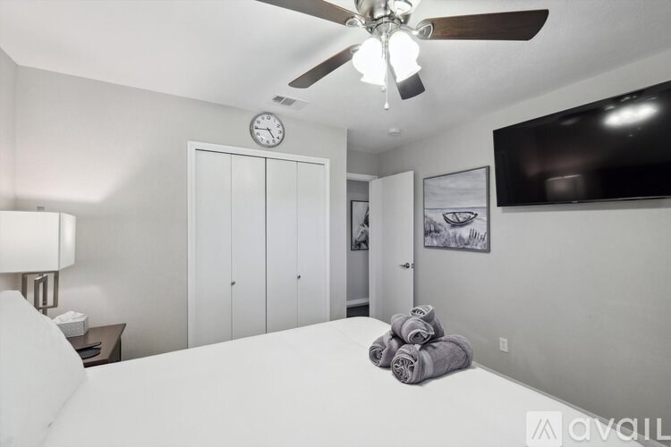 A bedroom with a bed, a ceiling fan, a clock, and a flat-screen TV mounted on the wall.