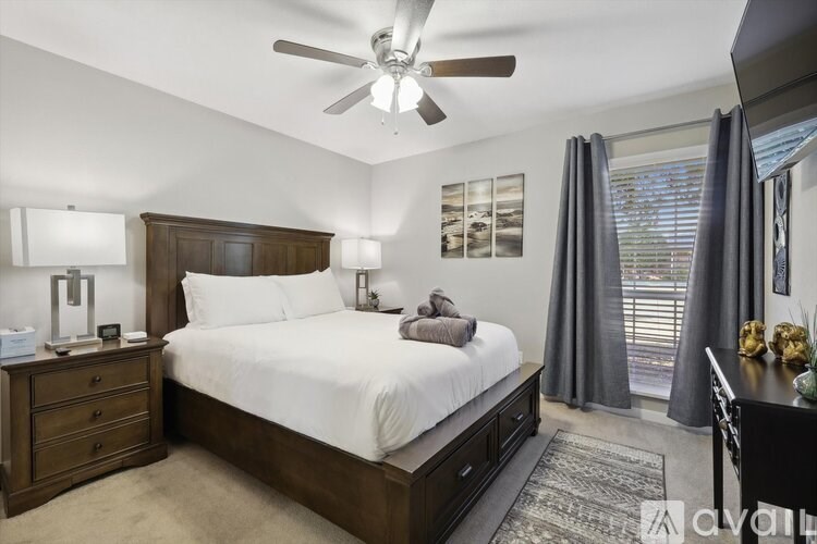 A bedroom with a large bed, a ceiling fan, and a nightstand with a lamp.