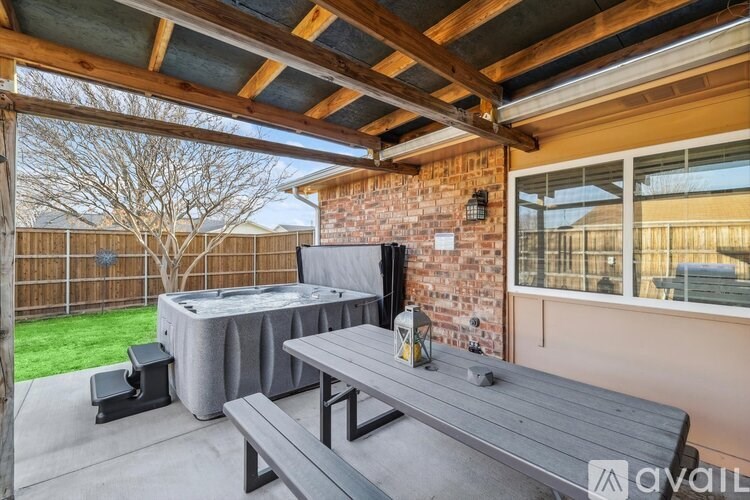 A patio with a hot tub, table, and bench under a wooden pergola.