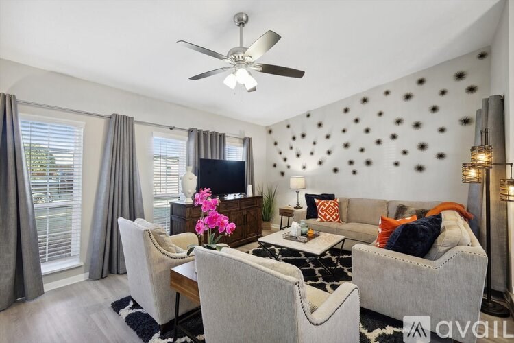 A living room with grey couches, a ceiling fan, and a wall with black dots.