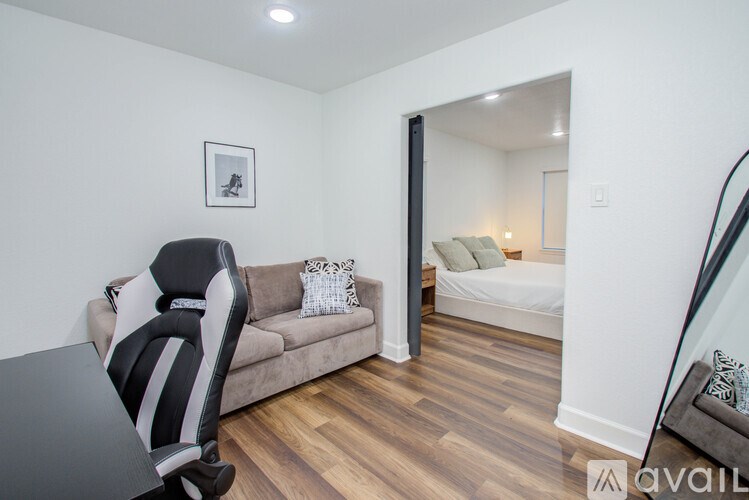 A black and white gaming chair is in the corner of a room with a couch and a picture on the wall.