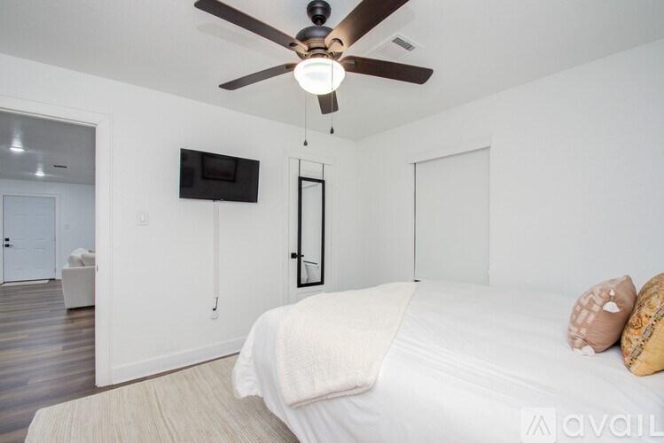 A bedroom with a bed, a ceiling fan, and a television mounted on the wall.