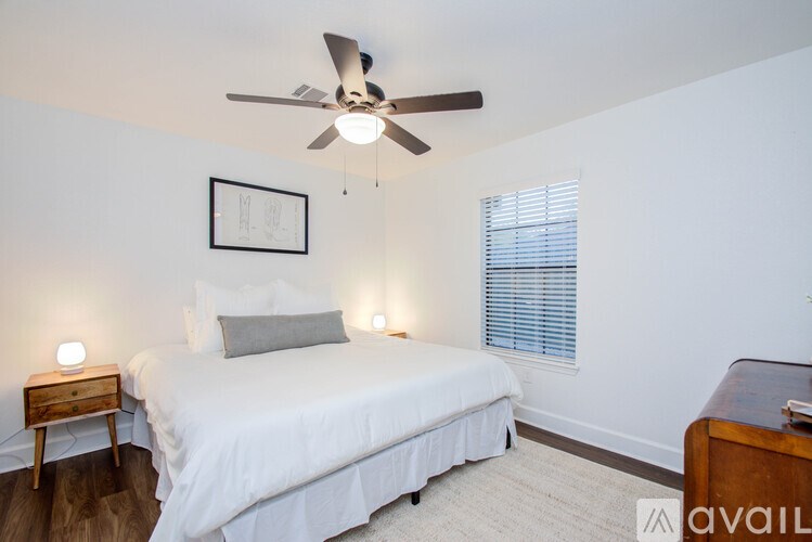 A bedroom with a bed, a ceiling fan, and a nightstand with a lamp.