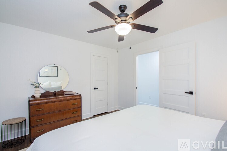 A bedroom with a white bed, a ceiling fan, and a dresser with a mirror on top.