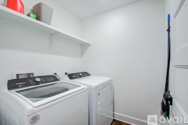 A white laundry room with a washer and dryer and a broom.