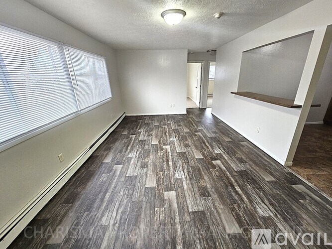 A room with wooden flooring and a window with blinds.