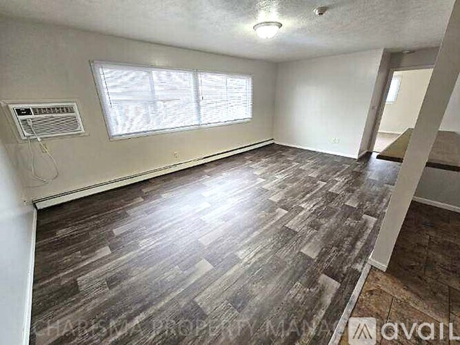 A room with wood flooring and a window with blinds.