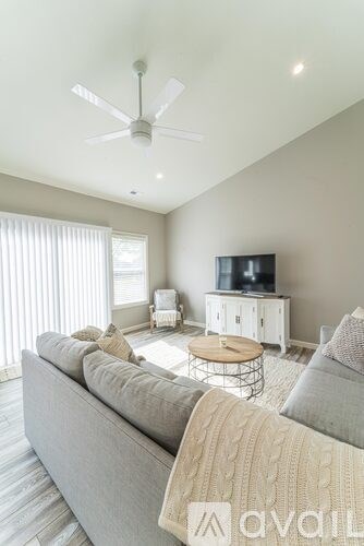 A living room with a grey sofa and a television on a white cabinet.