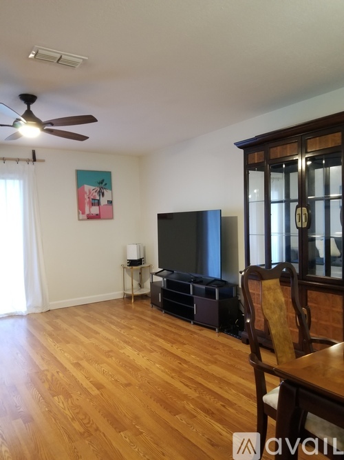A living room with a television, wooden floors, and a ceiling fan.
