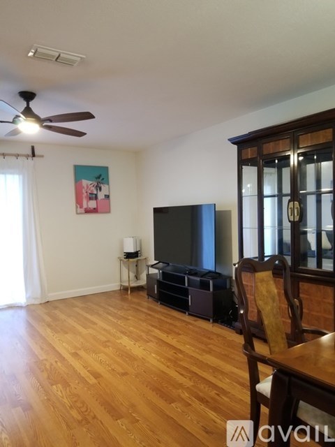 A living room with a television, wooden floors, and a ceiling fan.