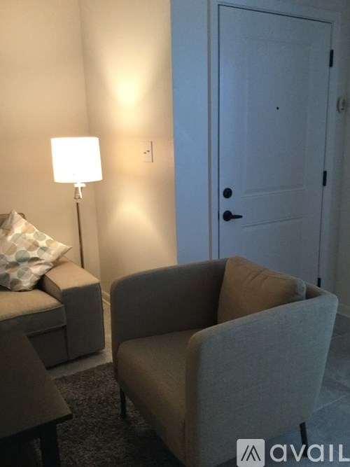 A lamp with a white shade is on a side table next to a couch.