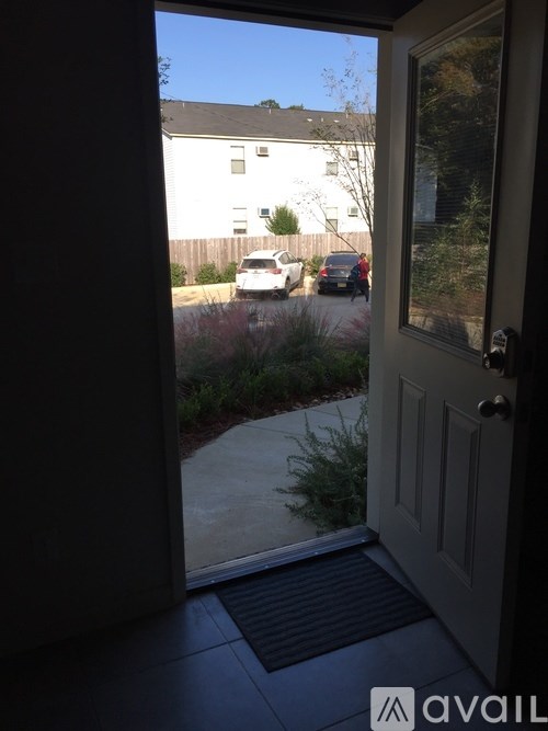 A white door with a glass window is open to a driveway with a white car and a brown fence.
