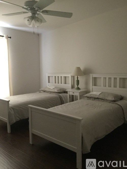 Two white beds in a room with a ceiling fan.