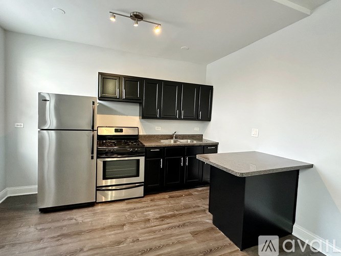 A kitchen with a stainless steel refrigerator, black cabinets, and a wooden island.