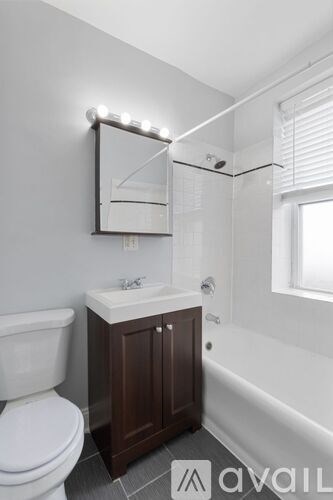A bathroom with a white toilet, a sink with a brown cabinet, and a white bathtub.