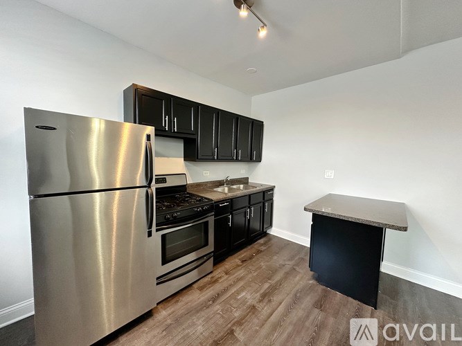 A kitchen with a stainless steel refrigerator, black cabinets, and a wooden floor.