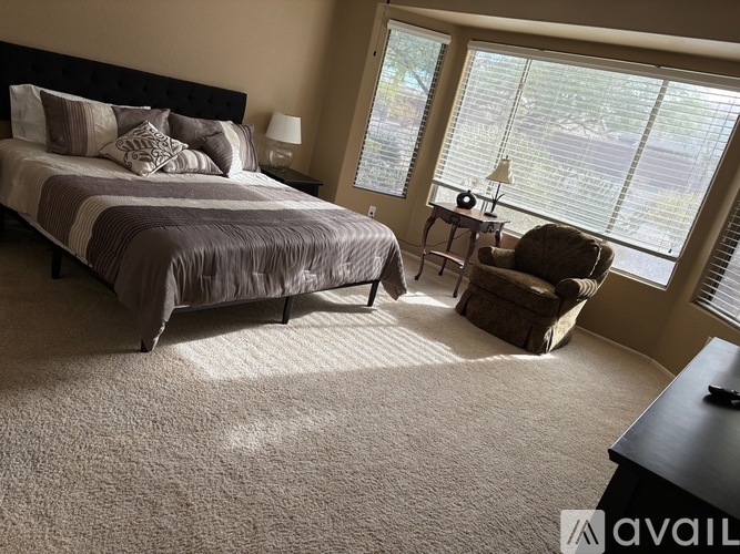 A bedroom with a large bed and a chair by the window.