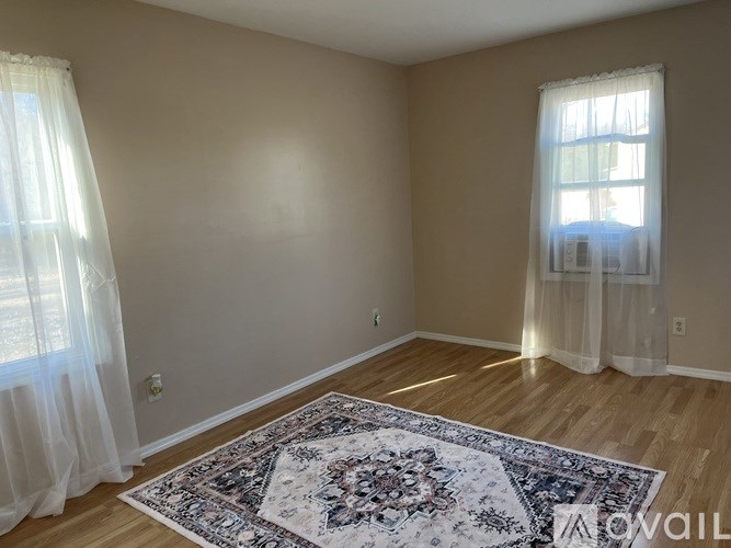 A room with a rug on the floor and a window with curtains.