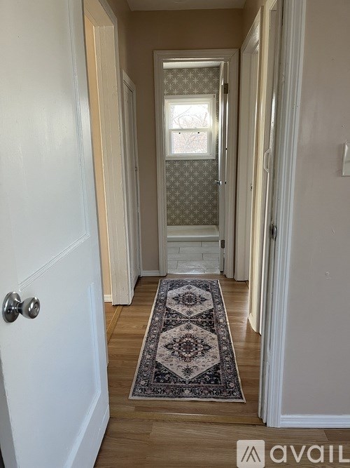 A hallway with a rug on the floor and a door on the left.