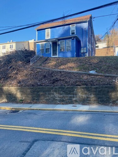 A blue house with a white door and windows is situated on a hill.