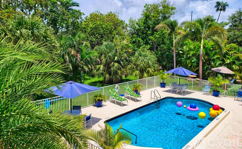 A pool surrounded by trees and a fence with chairs and umbrellas.