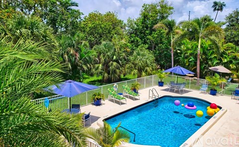 A pool surrounded by trees and a fence with chairs and umbrellas.