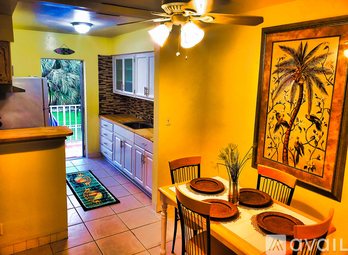 A kitchen with a table set for two with a palm tree picture on the wall.