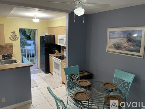A kitchen with a table set for two with a palm tree picture on the wall.