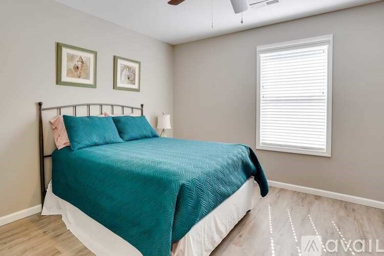 A bedroom with a bed, two pictures on the wall, and a window with blinds.