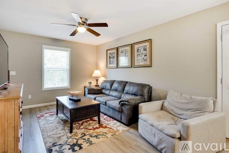 A living room with a black leather couch, a grey couch, a coffee table, and a ceiling fan.