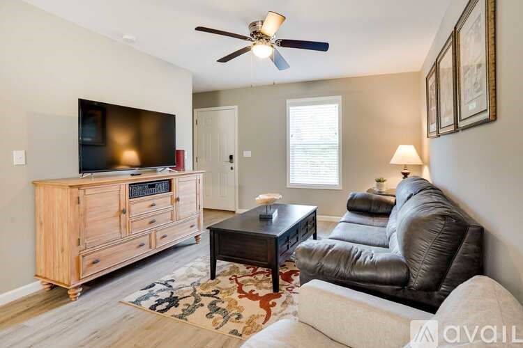 A living room with a black leather couch, a wooden cabinet, a flat screen TV, and a ceiling fan.
