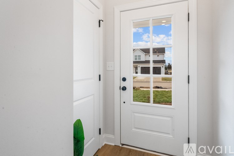 A white door with a glass window showing a house and a green chair in the foreground.