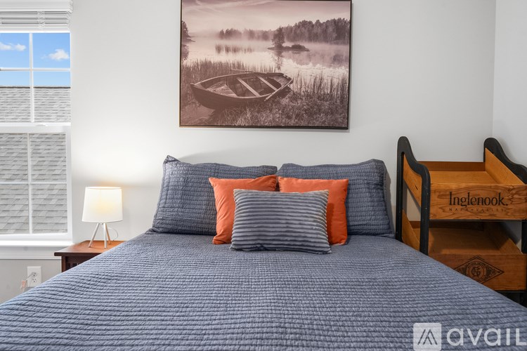 A bed with a blue comforter and pillows in front of a framed picture of a lake scene.
