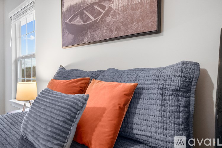 A bed with grey and orange pillows in a room with a framed picture on the wall.