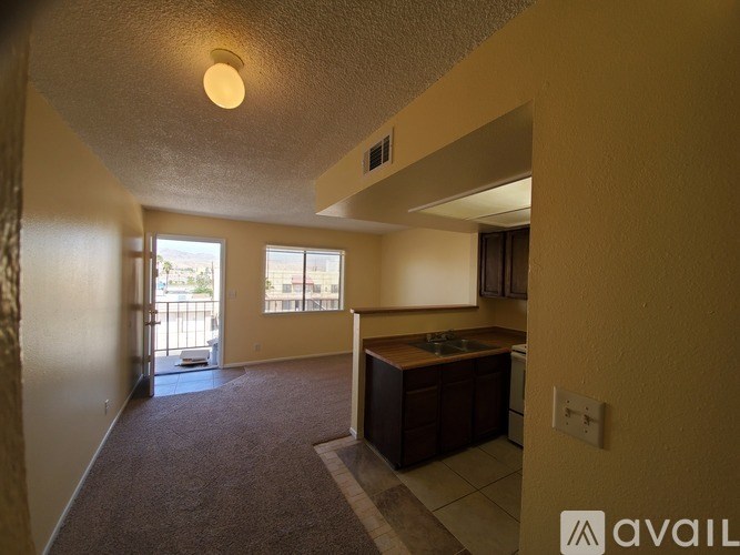 A room with a carpet floor and a kitchen area with brown cabinets.