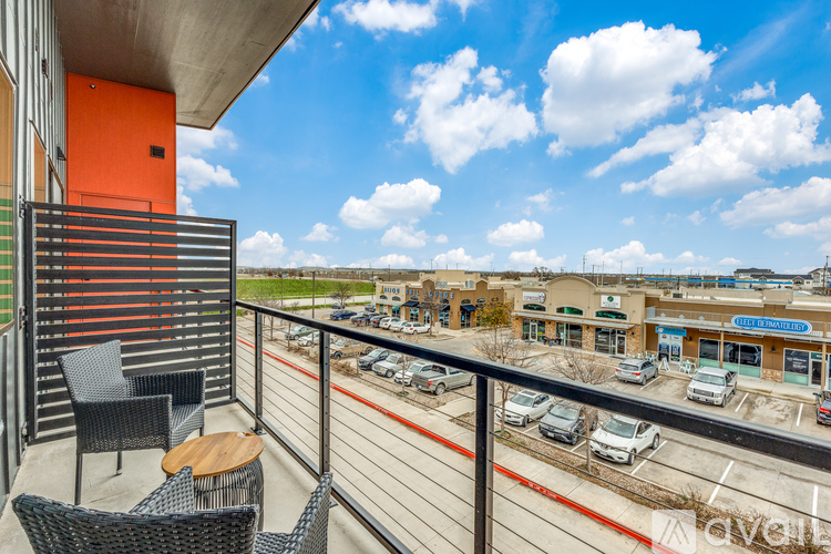 A balcony with chairs and a table overlooks a parking lot and buildings.