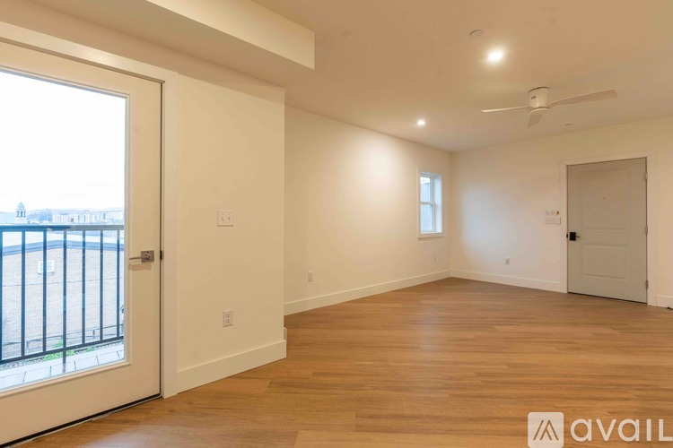 A spacious room with wooden floors and a view of a balcony with a railing.