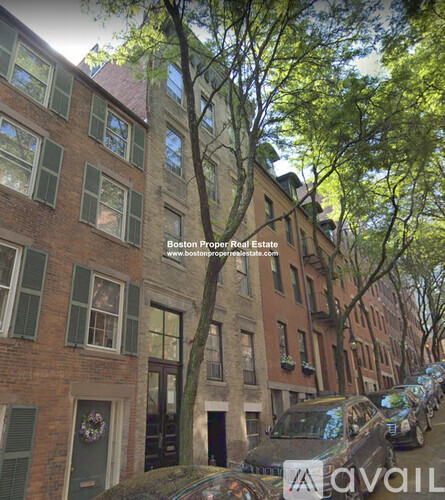 A row of brown brick buildings with green shutters and a tree in front of one of them.