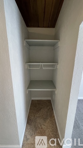 A white shelving unit with three shelves is in a corner of a room with a wooden ceiling.
