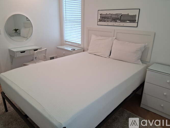 A white bedroom with a large bed, a dresser, and a mirror.