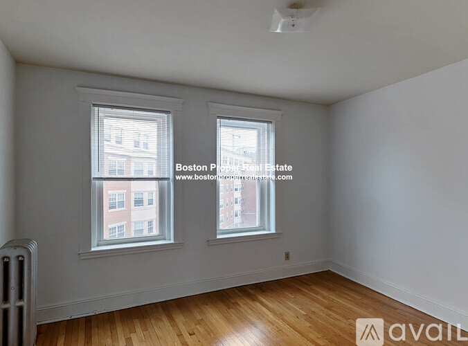 A room with wooden floors and two windows, one of which has a view of a building outside.