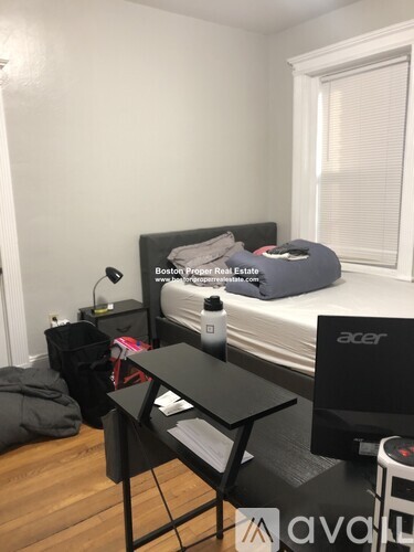 A bedroom with a bed, desk, and a window with blinds.