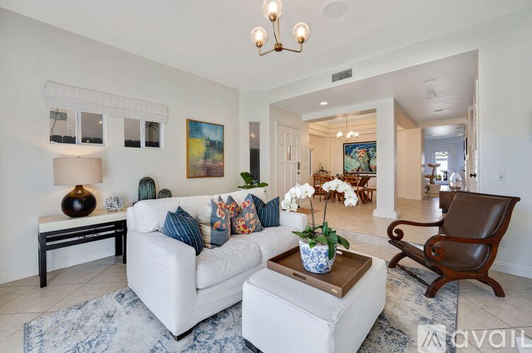 A living room with a white couch, a brown leather chair, and a chandelier.