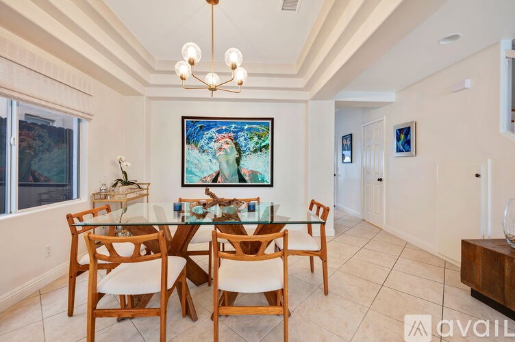 A dining room with a glass table and chairs, a chandelier, and a painting on the wall.